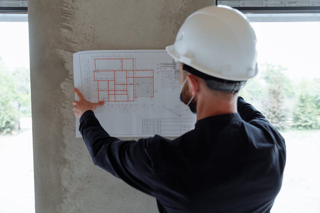 backview-of-an-engineer-holding-a-floor-plan-on-a-wall-8482551 aparejador en sevilla